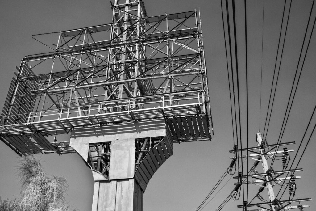 Schwarz-Weiß-Fotografie einer massiven Billboard-Konstruktion in Thailand, mit sichtbaren Stahlträgern und Stromleitungen im Vordergrund – Teil der Serie Billboards von J.F. Lindemann, Leica M und Summicron 28mm ASPH