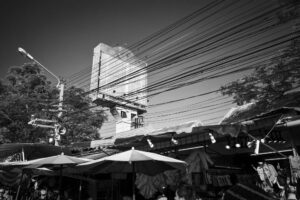 Bangkok, Thailand, Chatuchak Markt mit Sonnenschirmen und Reklametafel im Hintergrund, Stromleitungen, Schwarzweißfotografie, Serie BILLBOARD von J.F. Lindemann
