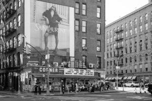 Schwarz-Weiß-Fotografie einer Straßenszene in New York City mit großem Saint Laurent Billboard über dem Corner Deli. Teil der Serie Billboards von J.F. Lindemann, Leica M, Summicron 28mm ASPH