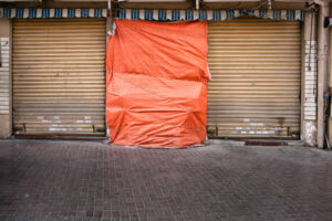 Geschlossene Ladenfront mit Rolltoren und oranger Plastikplane in Dubai – Fotografie aus der Serie FERMÉ-15 von J.F. Lindemann mit Leica M und Summicron 28mm ASPH