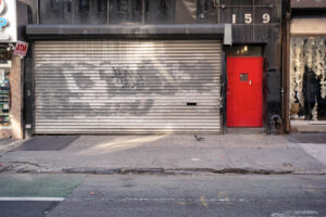 Geschlossenes Geschäft mit grauem Rolltor und roter Tür in New York City – Fotografie aus der Serie FERMÉ von J.F. Lindemann mit Leica M und Summicron 28mm ASPH