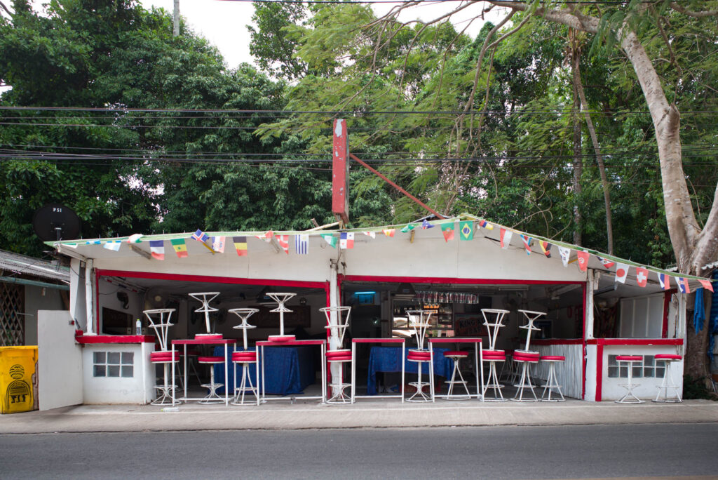 Geschlossene Bar mit hochgestellten roten Barhockern und bunten Fahnen in Koh Chang, Thailand – Fotografie aus der Serie FERMÉ-22 von J.F. Lindemann mit Leica M und Summicron 28mm ASPH