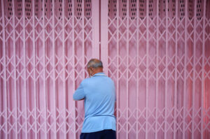 Mann in blauem Hemd schließt pinkfarbenes Rollgittertor in Thailand – Fotografie aus der Serie FERMÉ-4 von J.F. Lindemann mit Leica M und Summicron 28mm ASPH