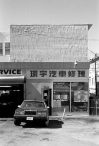 Schwarzweißfotografie eines geparkten Autos vor einem Laden mit asiatischer Beschriftung. fotografiert mit Leica M6 und Ilford FP4