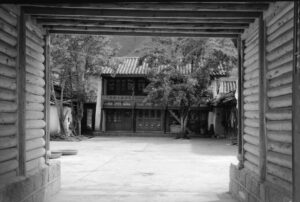 Traditioneller Hof einer Mosul Gemeinschaft am Lugu See in Yunnan, China, 1993, gesehen durch ein Holztor, Schwarzweiß-Fotografie mit Leica M6 und Summicron 35mm von J.F. Lindemann
