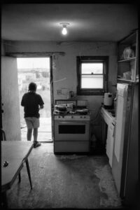 Küche mit Blick nach draußen, Junge steht in der Tür, Pine Ridge Reservat, South Dakota, Schwarzweiß-Fotografie von J.F. Lindemann, 1994