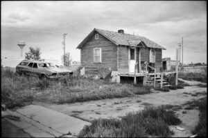 bewohntes Holzhaus mit Schrott-Auto im Pine Ridge Reservat, South Dakota, Schwarzweiß-Fotografie von J.F. Lindemann, 1994