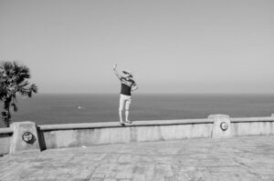 Tourist macht Selfie am Meer und balanciert auf einer Mauer; Schwarzweißfotografie mit Leica M und Summicron 28mm f/2.0 ASPH von J.F. Lindemann