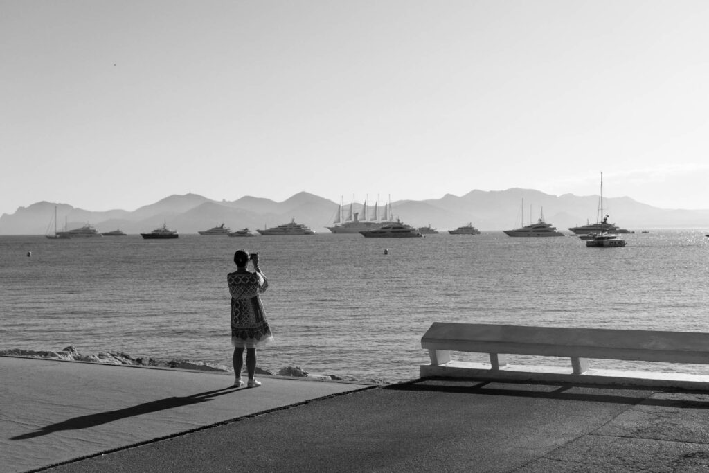 Frau fotografiert am Strand von Cannes, Frankreich, mit Blick auf das Meer und die Yachten. Schwarzweißaufnahme mit Leica M und Summicron 28mm f/2.0 ASPH von J.F. Lindemann.