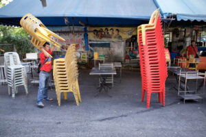 Straßenszene in Bangkok: Mann stapelt gelbe Plastikstühle neben einem hohen Stapel roter Stühle – Fotografie von J.F. Lindemann mit Leica M und Summicron 28mm ASPH