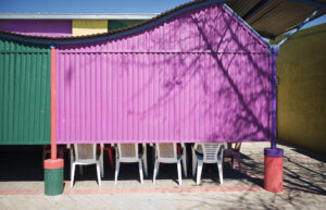 Vier weiße Plastikstühle im Schatten einer bunten Wellblechwand in Namibia – Fotografie von J.F. Lindemann mit Leica M und Summicron 28mm ASPH