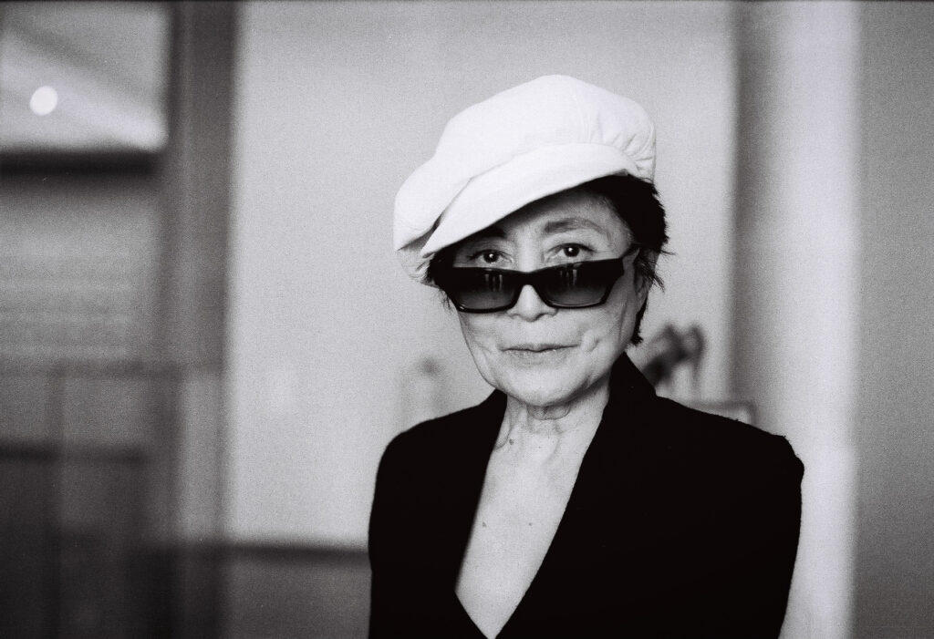 Yoko Ono mit Sonnenbrille und weißer Mütze, porträtiert von J.F. Lindemann mit Leica M6 und dem Summicron 35mm