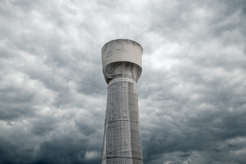 Verhüllter Turm vor dramatischem Himmel in Köln, flankiert von Überwachungskameras und Lautsprechern; Fotografie von J.F. Lindemann mit Leica M und Summicron 28mm f/2.0 ASPH, Serie WRAPPED