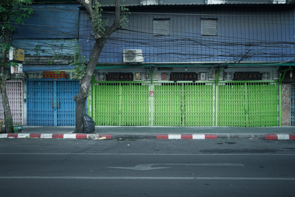 Geschlossene Ladenfronten mit blauen und neongrünen Rollgittern in Bangkok – Fotografie aus der Serie FERMÉ-14 von J.F. Lindemann mit Leica M und Summicron 28mm ASPH