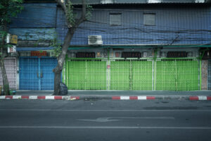 Geschlossene Ladenfronten mit blauen und neongrünen Rollgittern in Bangkok – Fotografie aus der Serie FERMÉ-14 von J.F. Lindemann mit Leica M und Summicron 28mm ASPH