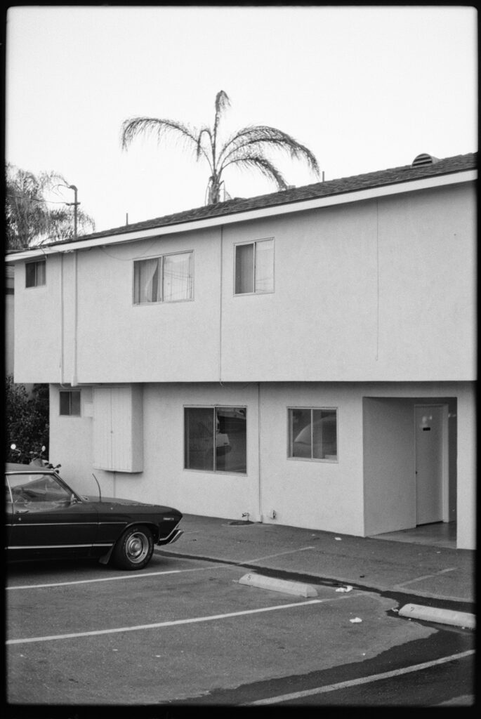 Apartmentgebäude mit geparktem Oldtimer in Palm Springs, Schwarzweißfotografie aufgenommen mit Leica M6 und Summicron 35mm auf Ilford HP4 Film, Fine Art Print von J. F. Flindemann