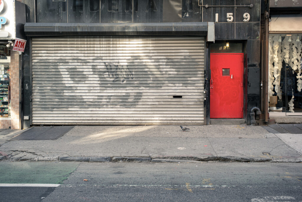 Geschlossenes Geschäft mit grauem Rolltor und roter Tür in New York City – Fotografie aus der Serie FERMÉ von J.F. Lindemann mit Leica M und Summicron 28mm ASPH