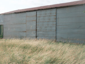 Großes Metallgebäude mit geschlossener Fassade in Electra, Texas. Davor Gräser.