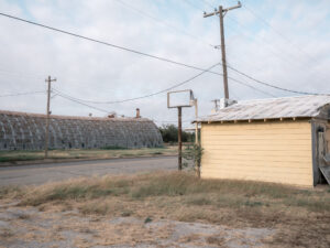 Kleines Nebengebäude mit Holzwand vor Industriehallen in Electra, Texas.