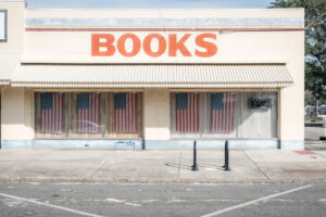 Ladenfassade mit Schriftzug „Books“ und leeren Schaufenstern in Saint Petersburg, Florida. Im Fenster sieht man die amerikanische Flagge und den Schriftzug open.